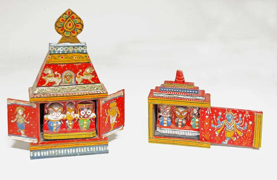 Zwei reich mit indischen Verzierungen, Löwen und Göttern bemalte, kleine Tempel aus Holz. Sie sind aufgeklappt und zeigen innen drei bunte Figuren mit großen Augen.