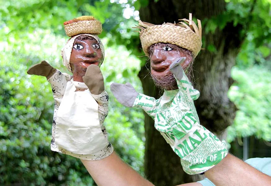 Zwei Handpuppen mit Stoffkörper und Köpfen aus bemaltem Ton. Es sind eine Frau mit Kopftuch und ein Mann mit Barthaaren. Beide haben einen aus Bast geflochtenen Kob auf dem Kopf.