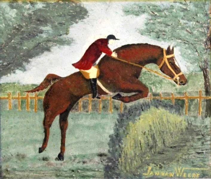 Ein Reiter mit rotem Jacket, schwarzer Reiterkappe und Reitstiefeln sitzt vorgebäugt auf einem großen braunen Pferd im Sprung über ein Naturhinderniss. Im Hintergrund ein Zaun und grüne Bäume.